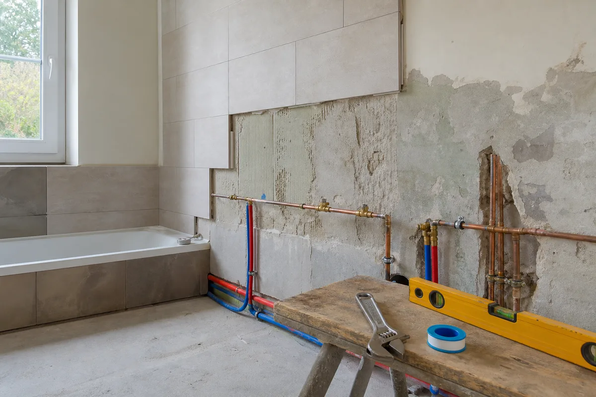 Salle de bain en cours de rénovation avec tuyauterie apparente et outils de plomberie