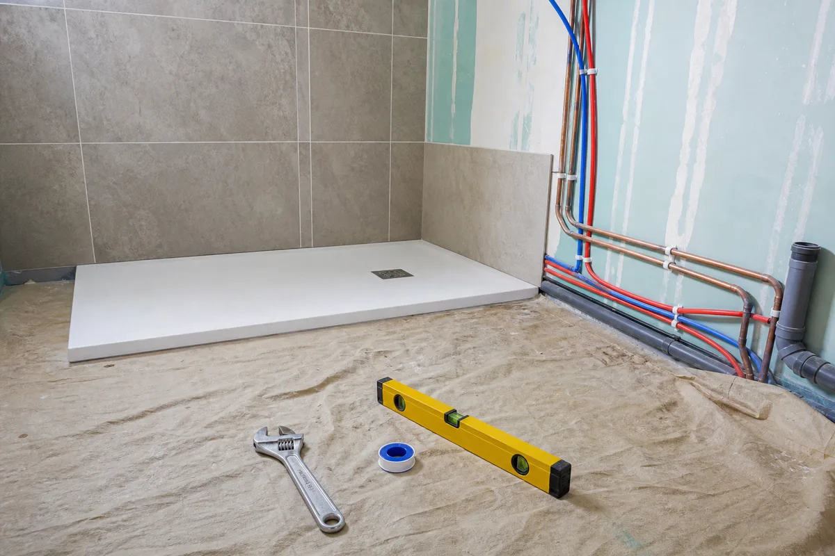 Salle de bain en chantier de rénovation avec receveur de douche et tuyauterie apparente